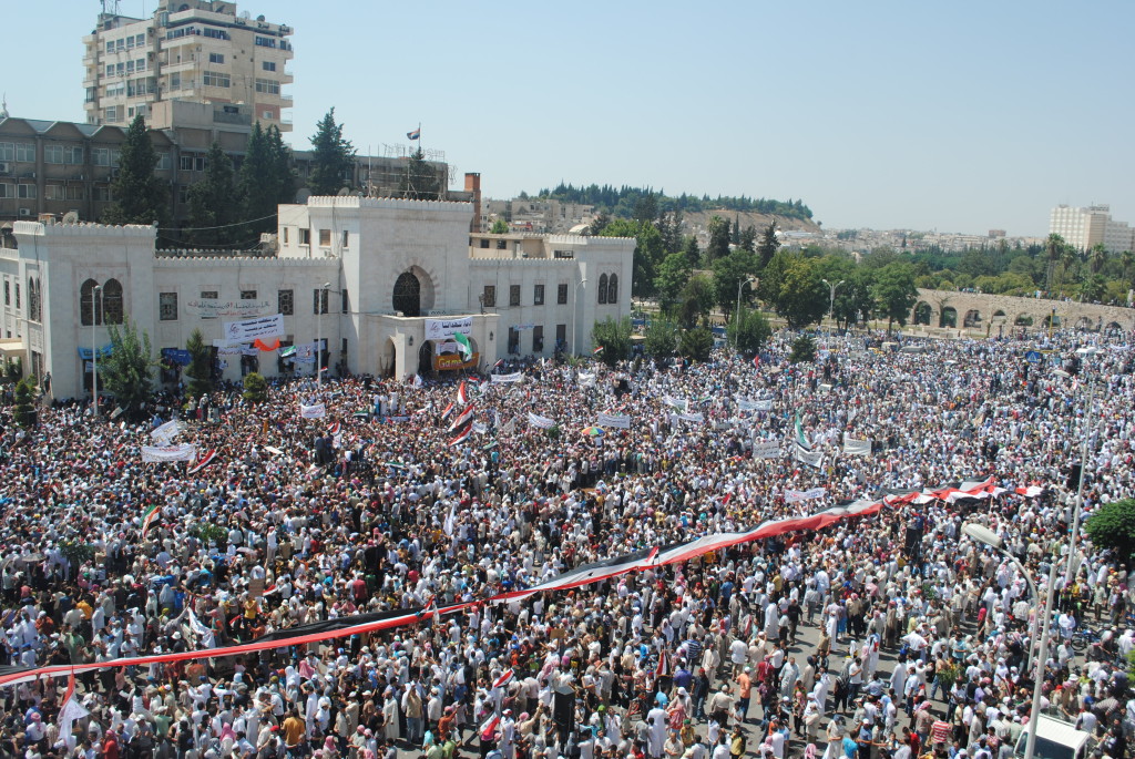 Protesta antigovernativa ad Hama, primi mesi del 2011; la bandiera della Rivoluzione con la fascia verde anziché rossa venne adottata da luglio in poi per distinguersi da quella del governo siriano, ancora in uso nelle primissime proteste. Credit to: ABC News