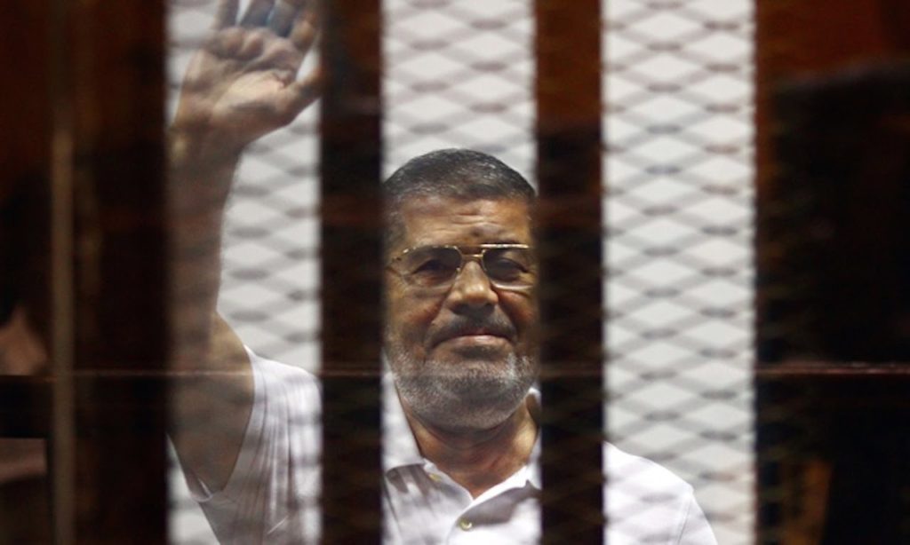 L'ex presidente egiziano Mohammed Morsi saluta i presenti durante un'udienza al Tribunale del Cairo. Credits: AHMED OMAR / AP