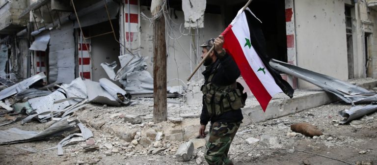 Un soldato siriano sventola la bandiera siriana nel quartiere di Aleppo est di Tariq al-Bab. Credits to: Hassan Ammar/AP