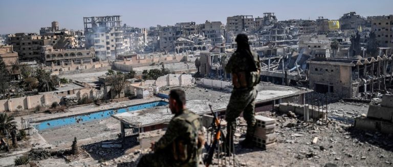 Combattenti delle SDF osservano le macerie di Raqqa dopo la liberazione. Credits to: Bülent Kılıç/AFP/Getty Images.
