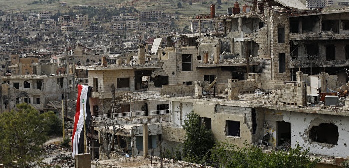 Una bandiera nazionale siriana pende da un edificio danneggiato nella località montana di Zabadani (Damasco), 18/05/2017. Credits to: Hassan Ammar/AP.